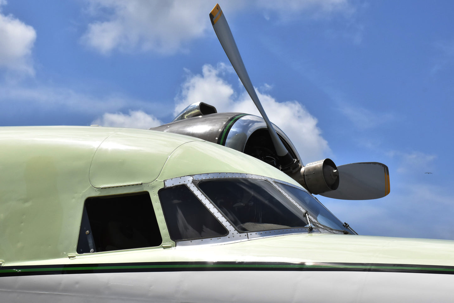 Close-up of a propeller on a light green aircraft against a blue sky with clouds.
