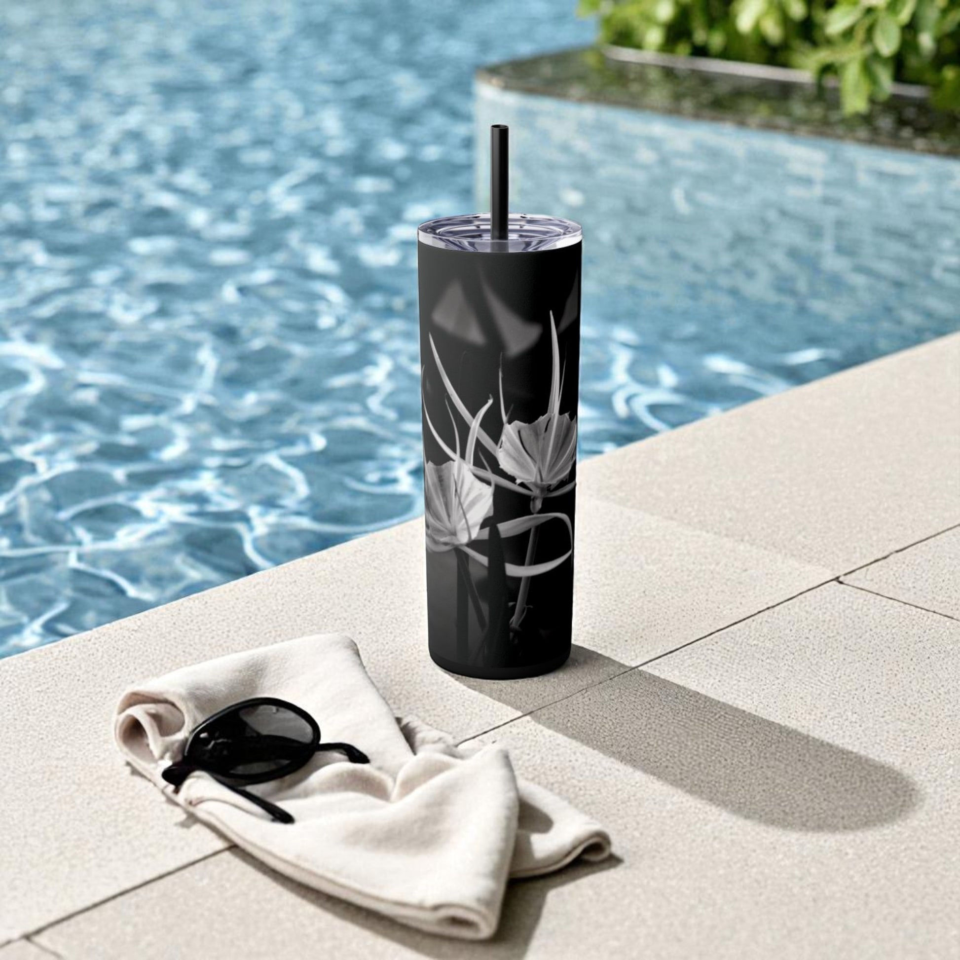 Black tumbler with floral design on a towel by a pool