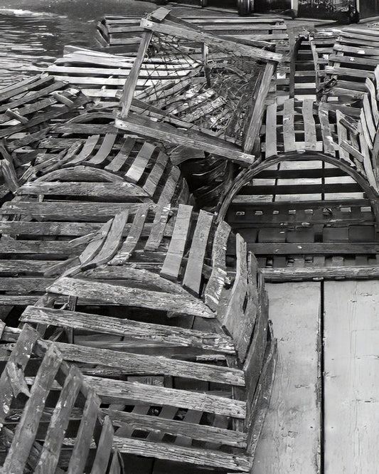 A black and white photograph of old wooden lobster traps arranged neatly on the ground, showcasing their weathered texture. Lobster Traps Original Black and White Photograph by Kim A. Bailey