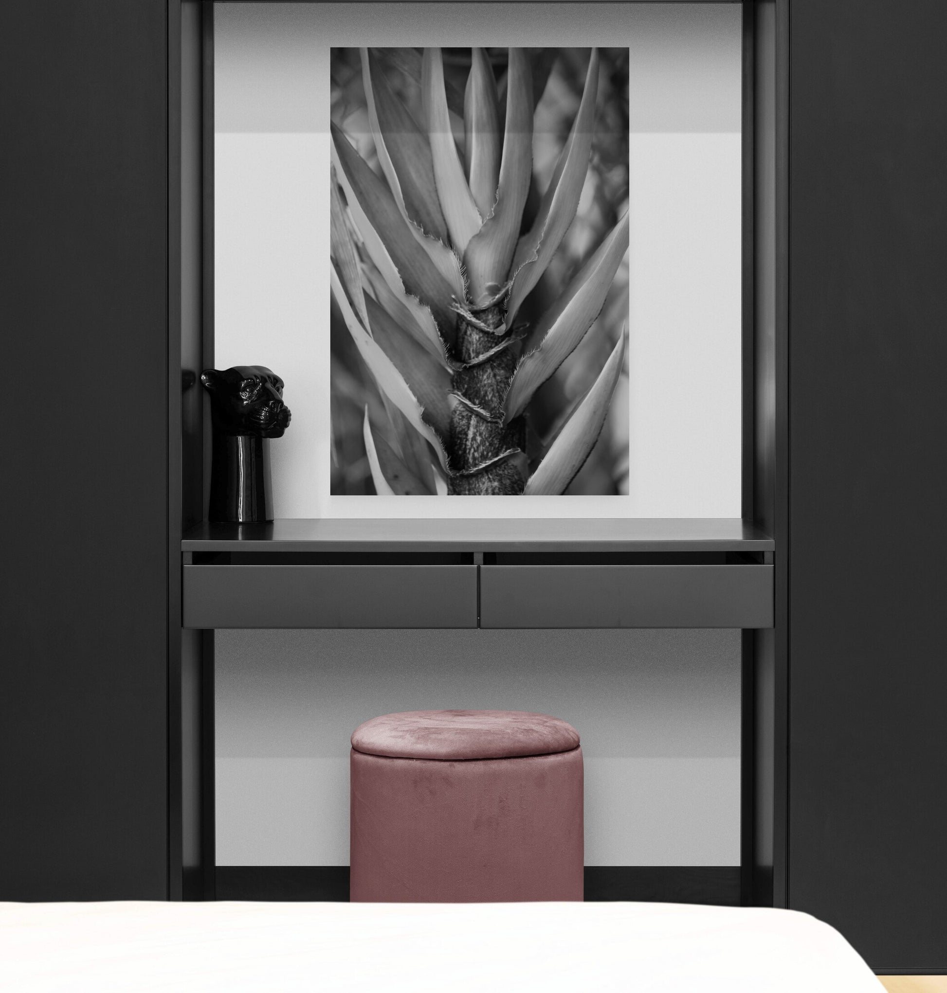 Modern interior with a black and white abstract art piece on a wall, a pink stool, and a dark cabinet.