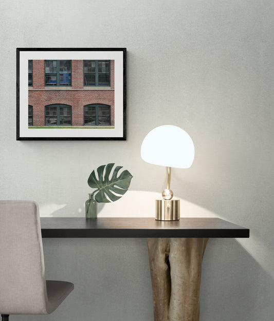 Modern desk with lamp and plant against a gray wall with a framed picture. 