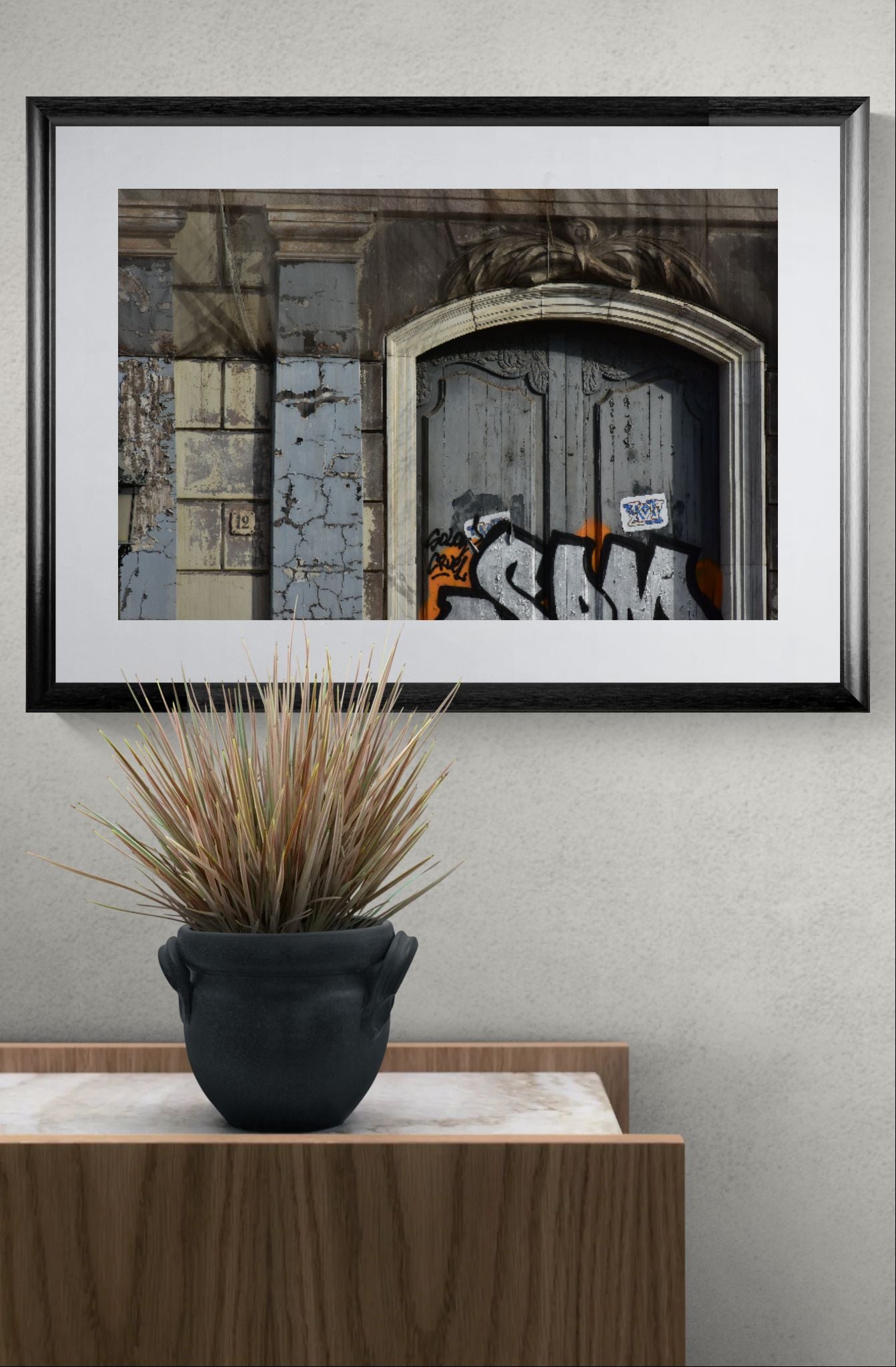 Framed artwork on a wall with a plant below