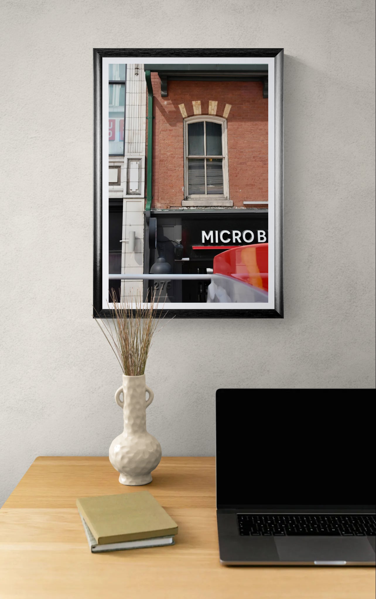 A brick building facade with a single arched window above a storefront sign reading MICRO B, shown in an urban street setting. Framed photograph hanging over a home office space.