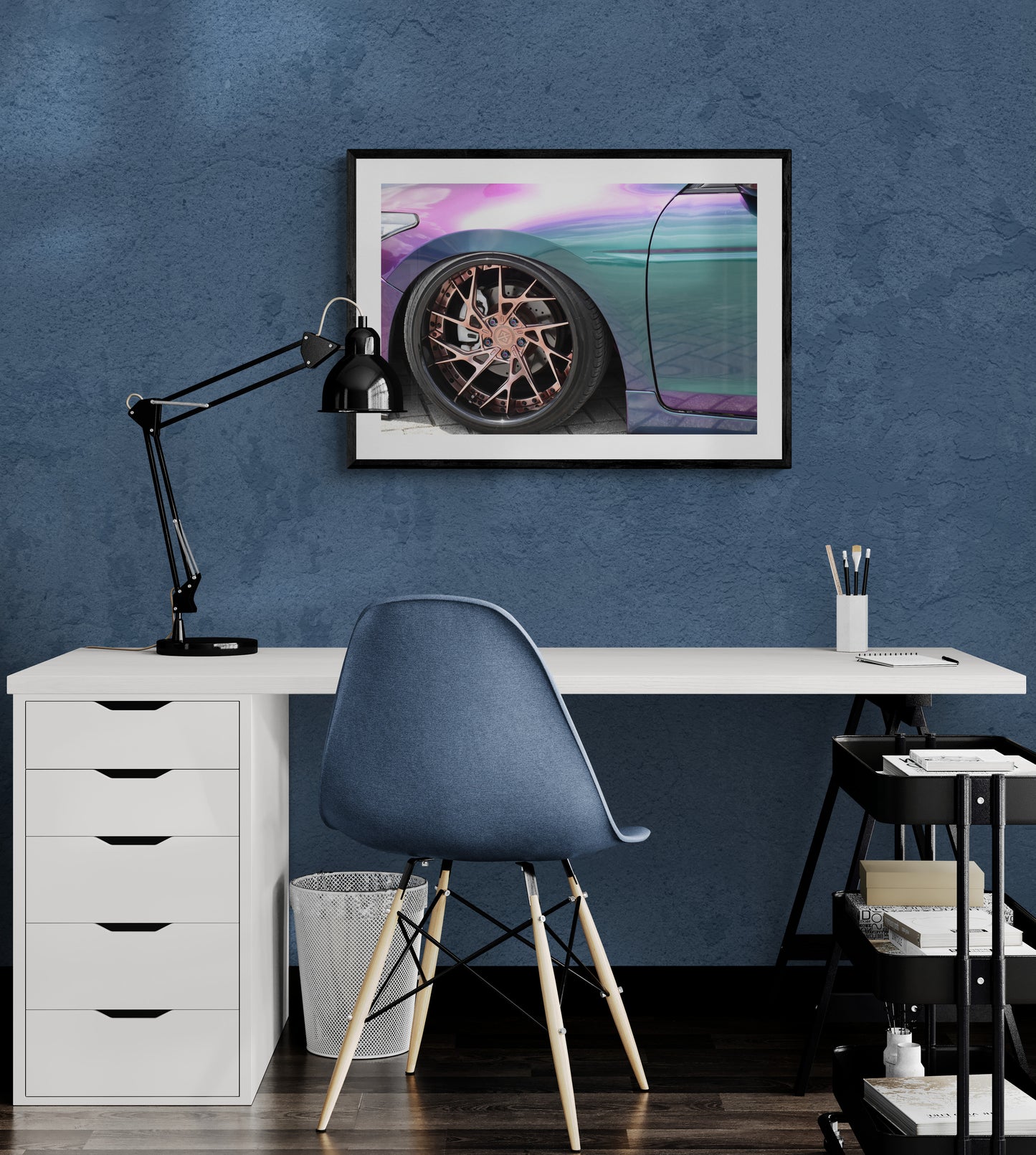 Modern office setup with a desk, chair, lamp, and framed picture on a blue wall.