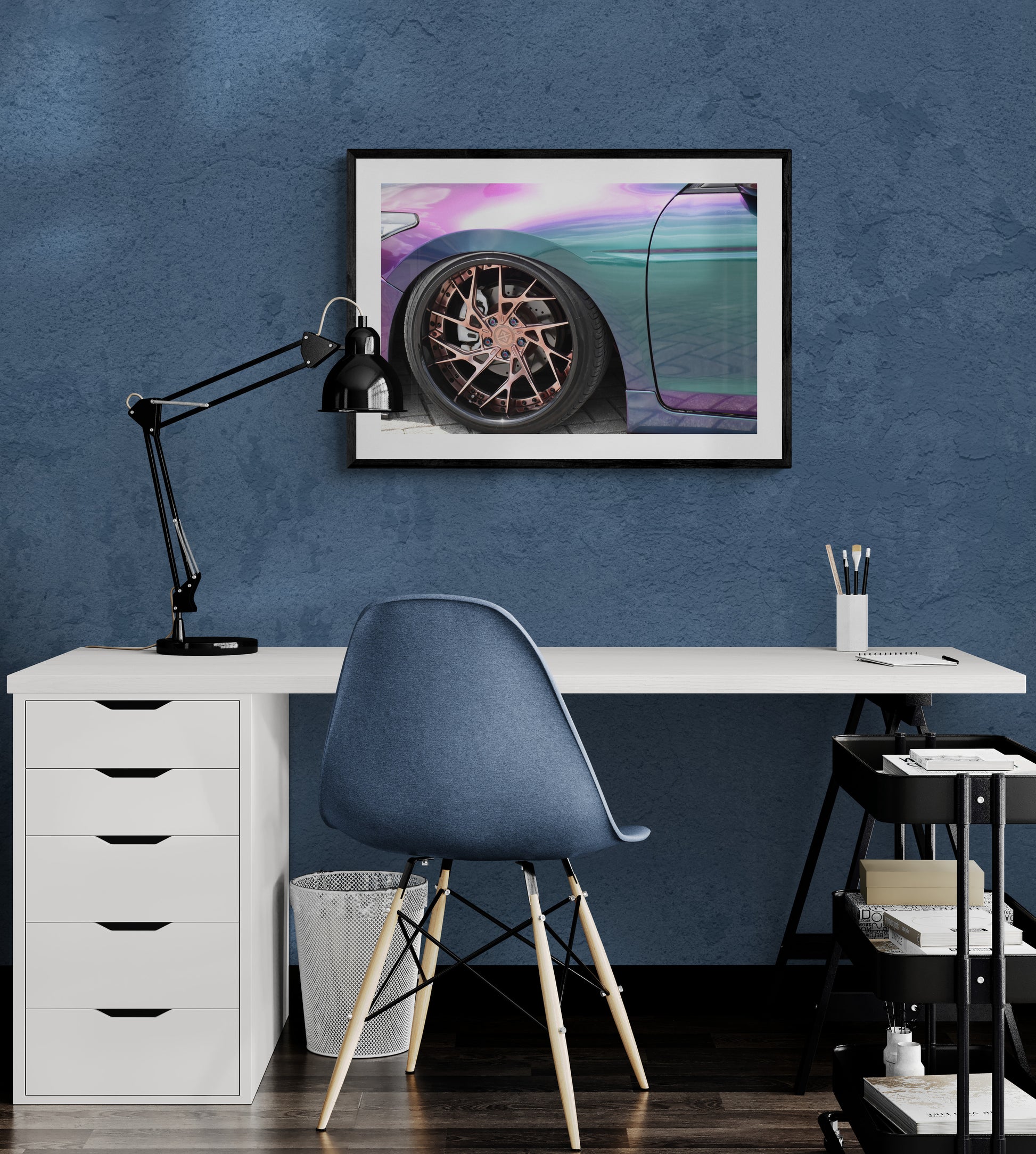 Modern office setup with a desk, chair, lamp, and framed picture on a blue wall.