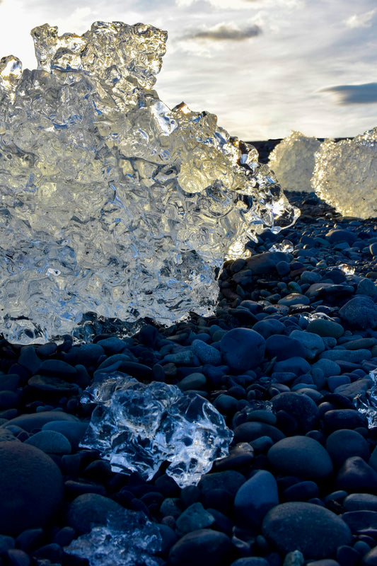 Icebergs washed ashore on a black volcanic sand beach, with the remains of ice chunks in the foreground, creating a sparkling effect in the sunlight.