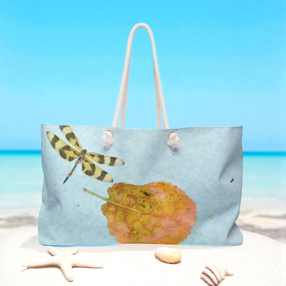 Beach bag with a dragonfly and leaf design on a beach setting