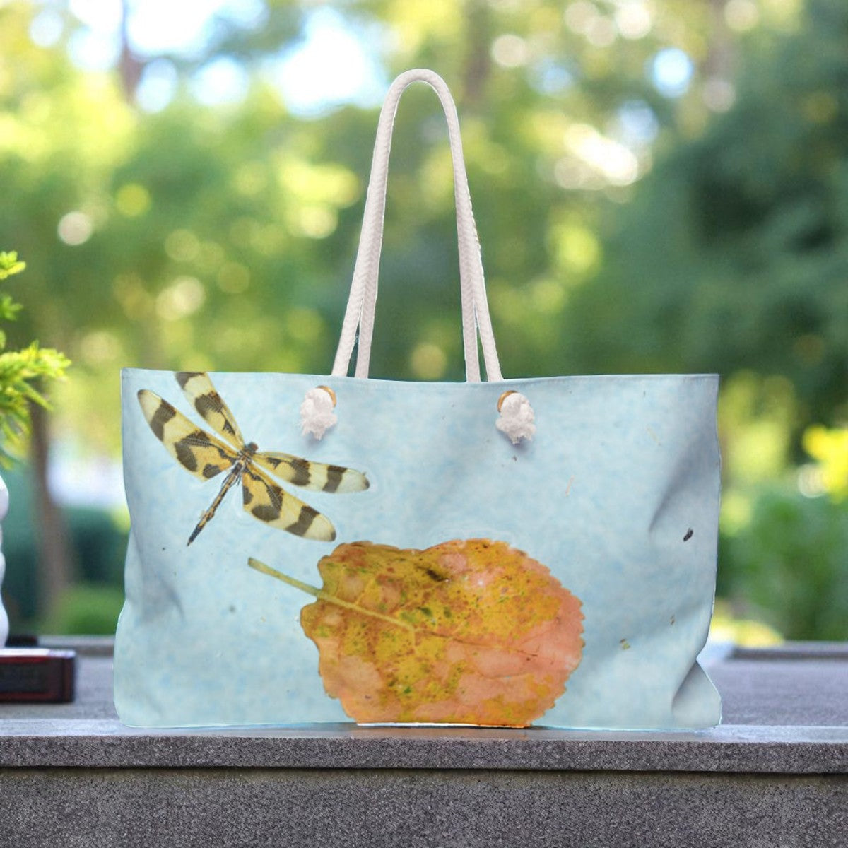 Tote bag with a dragonfly and leaf design on a blurred natural background