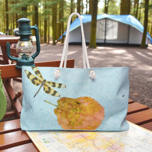 Tote bag with a dragonfly design on a table in a forest setting