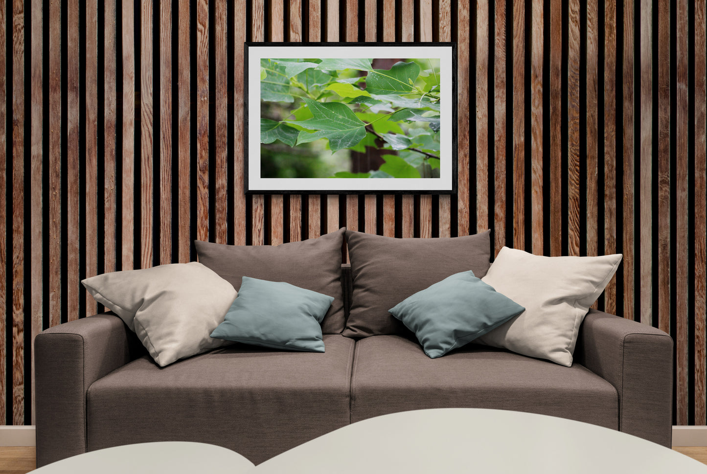 Brown sofa with decorative pillows against a wooden wall with a leafy plant artwork.