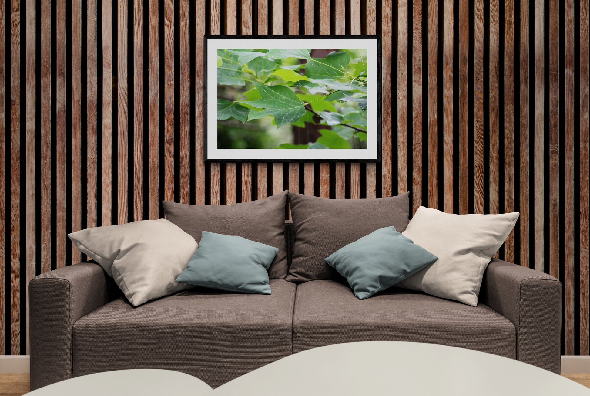 Brown sofa with decorative pillows against a wooden wall with a leafy plant artwork.