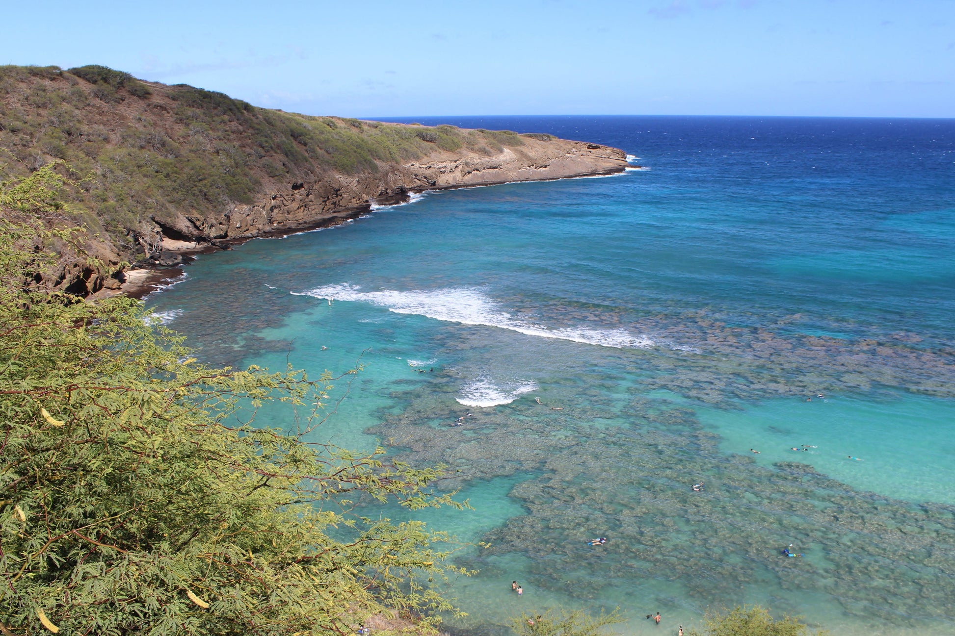 A photograph of Hanauma Bay with clear blue water, a crescent-shaped bay, and a lush green shoreline. Hanauma Bay Surf Original Photograph by Kim A. Bailey