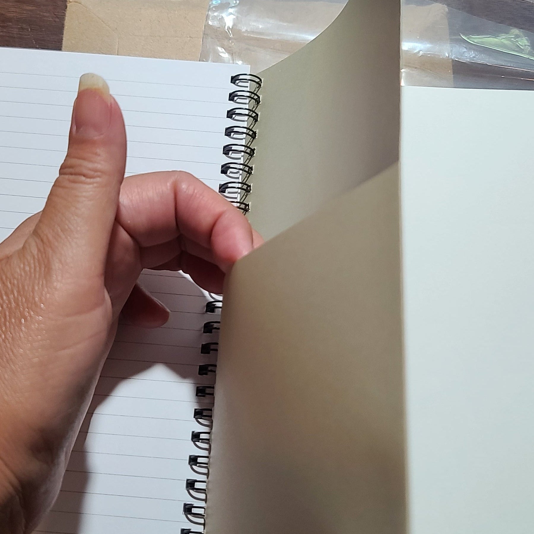 Hand holding a spiral-bound notebook against a wooden surface