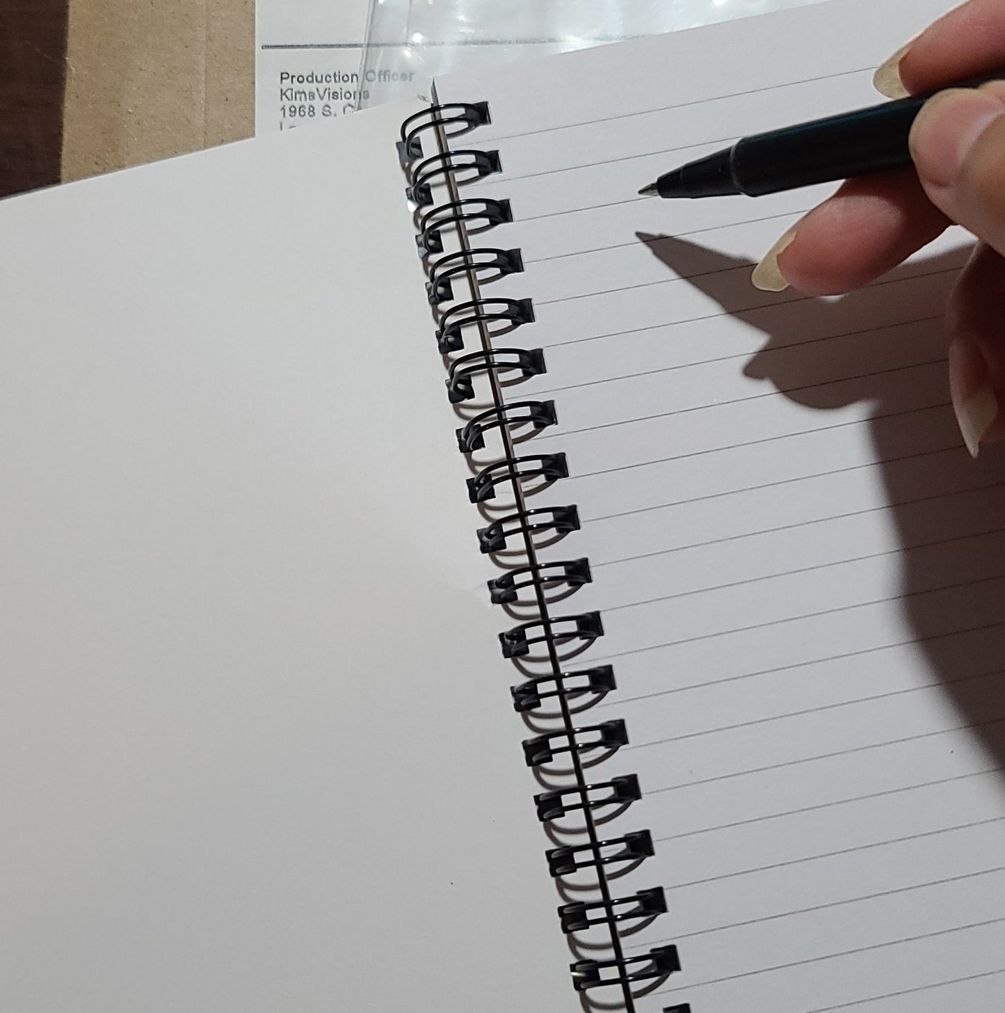 Person holding a pen over a spiral-bound notebook on a wooden surface
