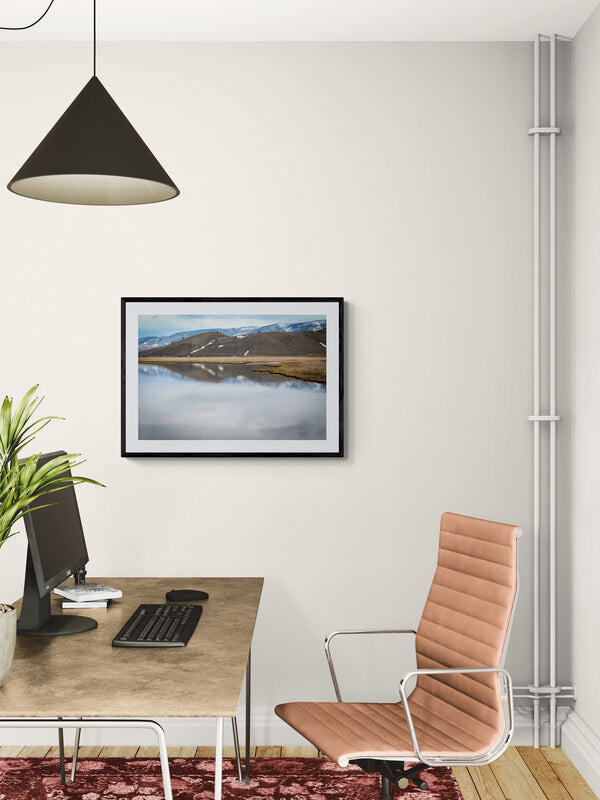 Modern office setup with a desk, chair, and framed landscape picture on a white wall.