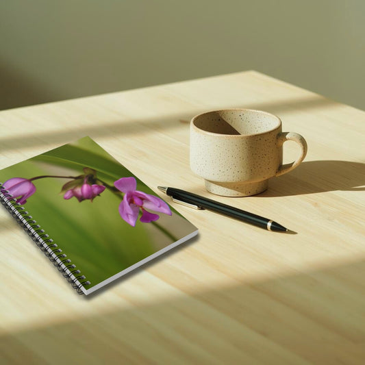 Notebook with floral design, cup, and pen on a wooden surface