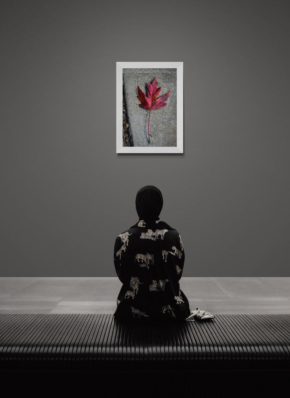 Person sitting on a bench in a room with a framed picture of a red leaf on a gray wall.