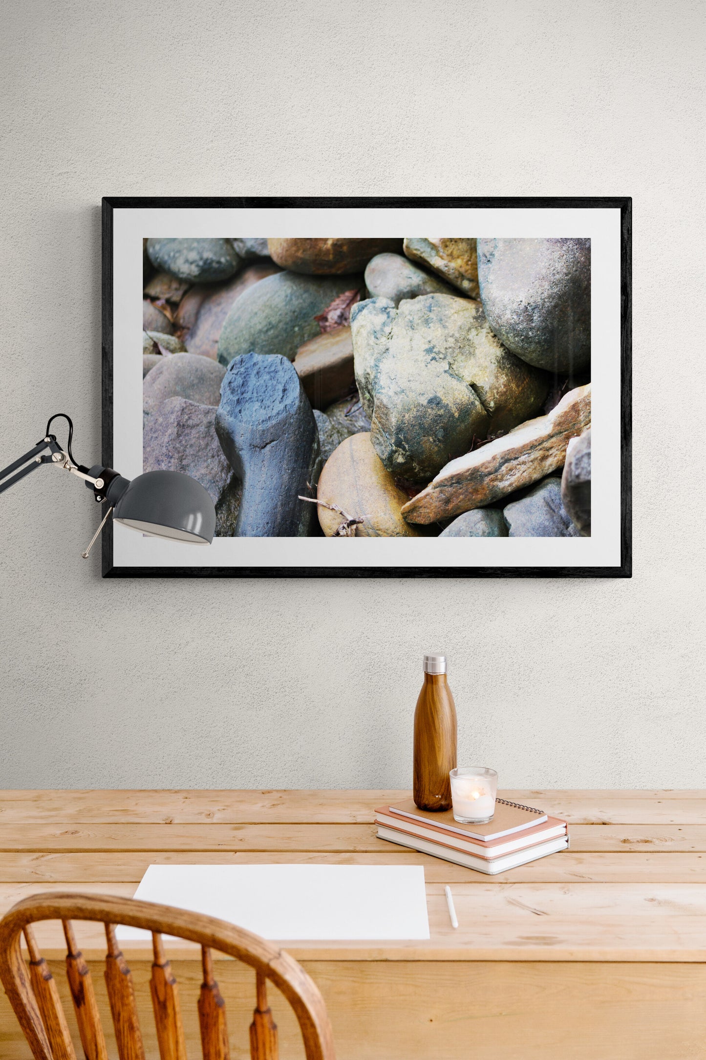 Framed photograph of rocks above a wooden desk with a lamp and bottle.