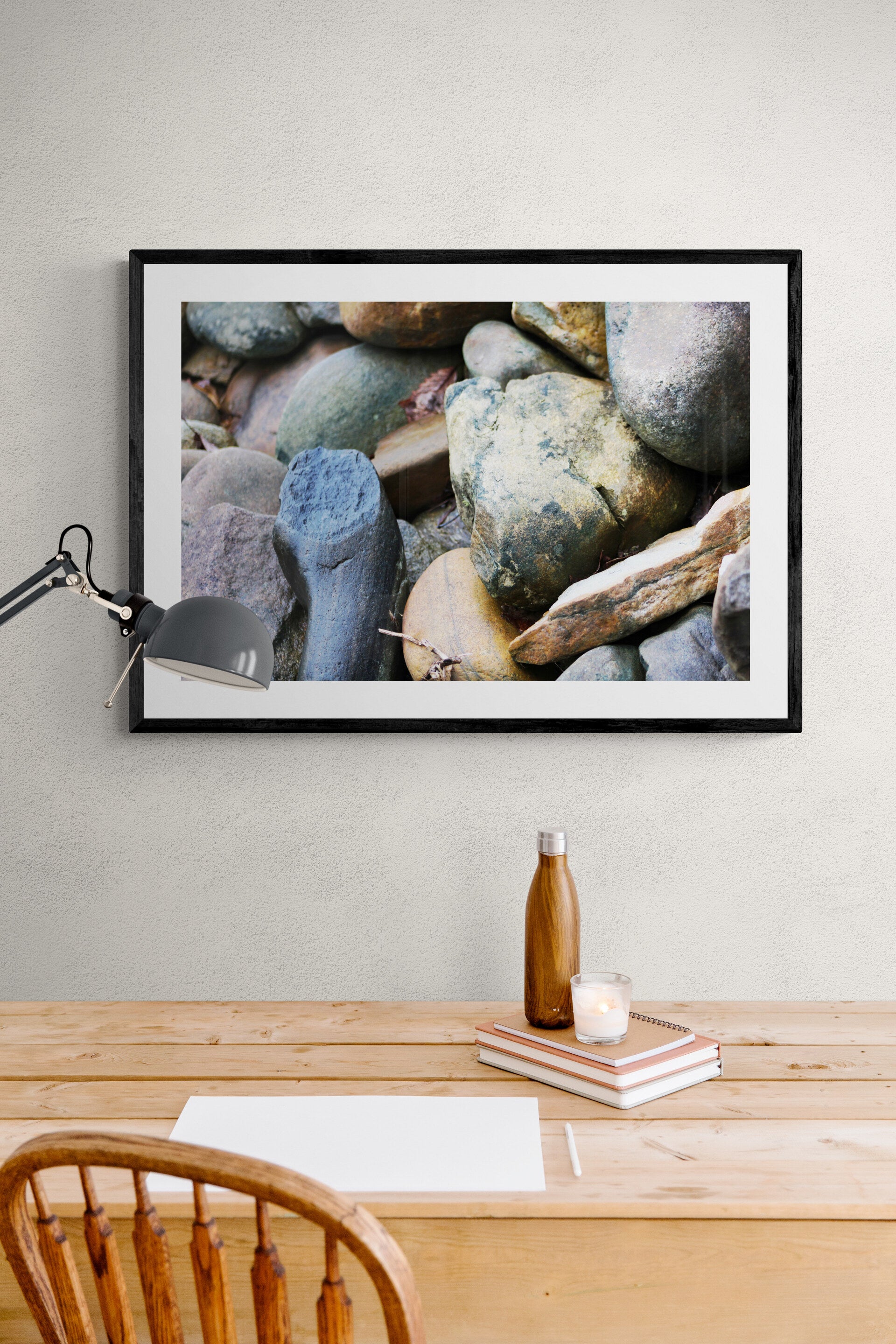 Framed photograph of rocks above a wooden desk with a lamp and bottle.