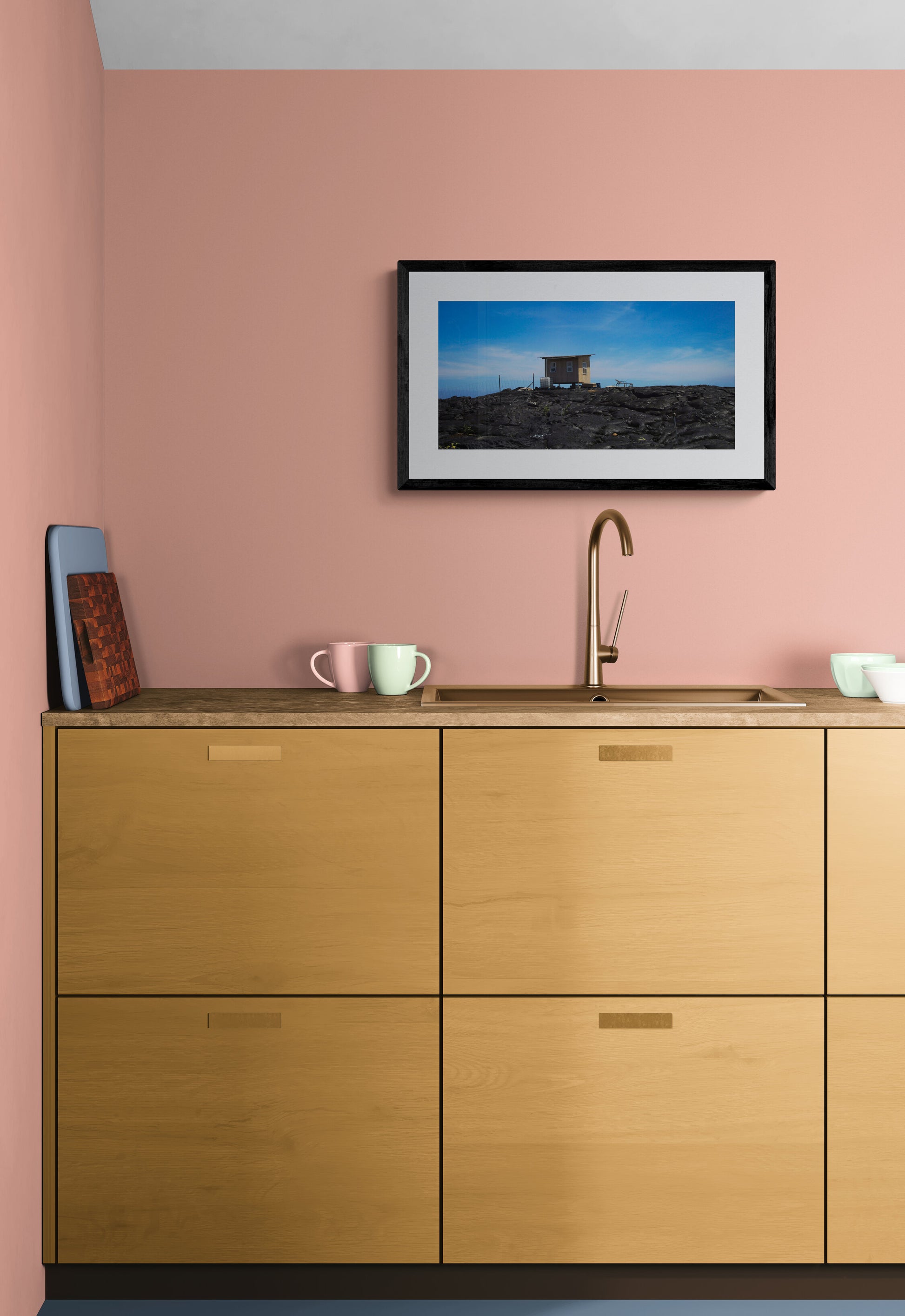 Wooden kitchen cabinets with a pink wall and framed picture above.