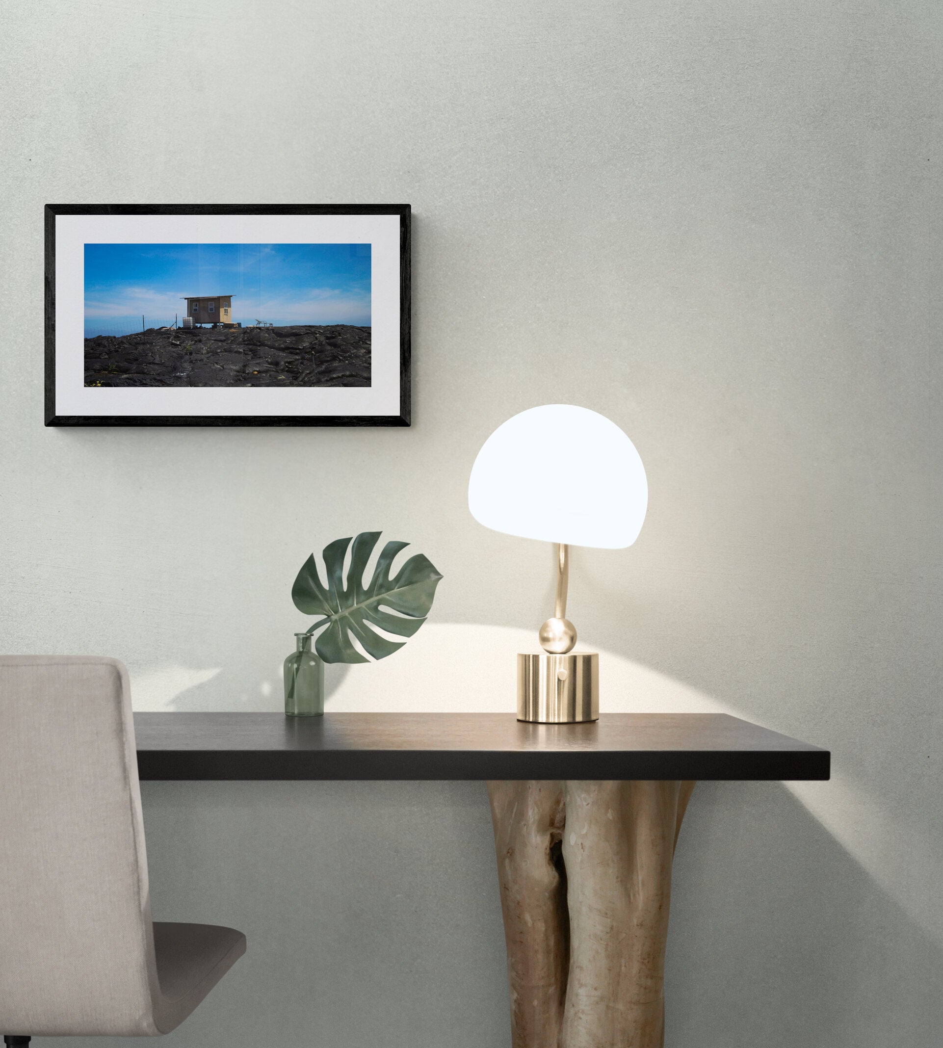 Modern desk setup with a lamp, plant, and framed picture against a neutral background.