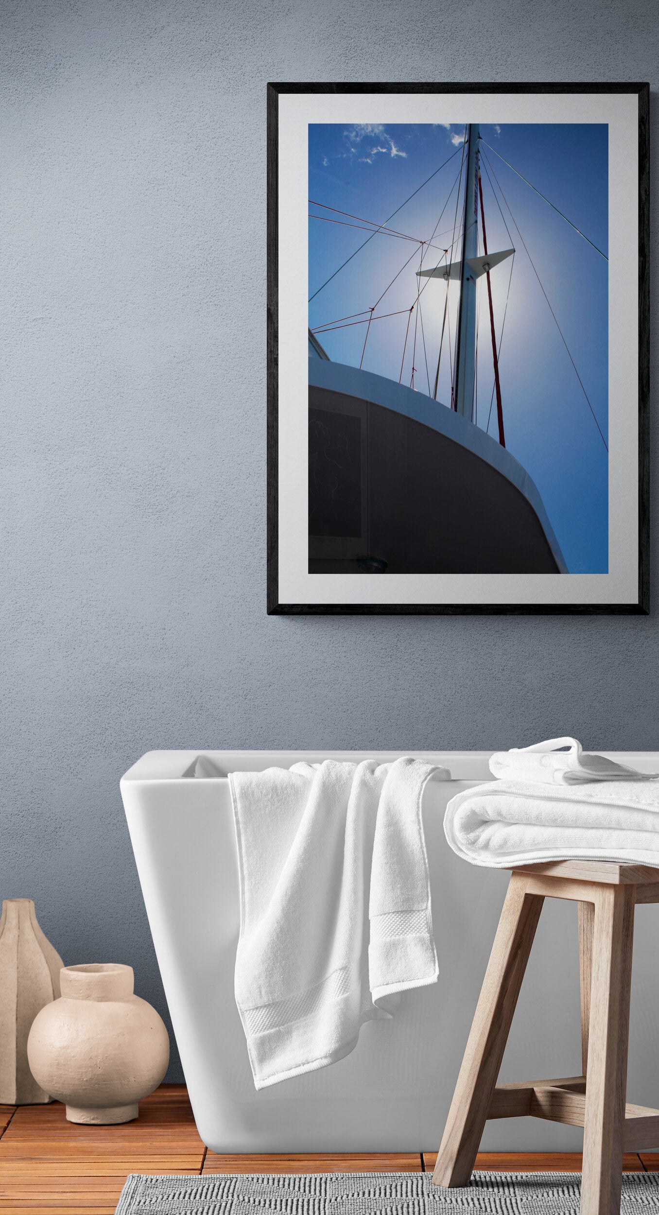 Framed photograph of a ship's mast against a blue sky above a bathtub with white towels.