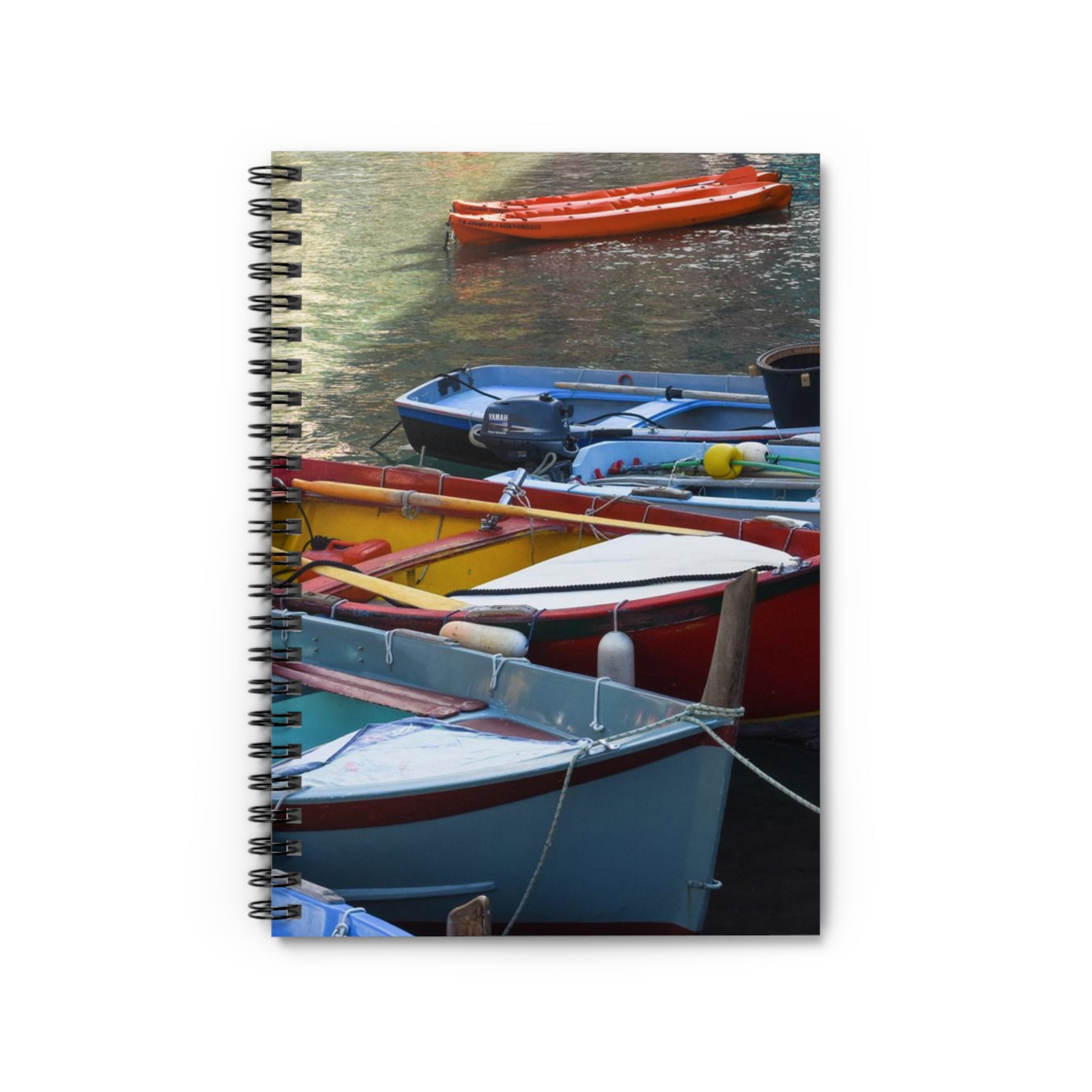 A spiral notebook with a front cover print of colorful fishing boats on water, with a dark grey back cover.