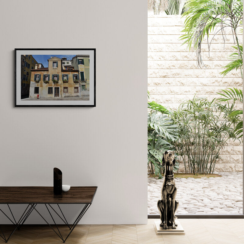 Interior with a framed photo of a building, plant-filled courtyard, and statue on a table. Venice Residence, Original Photograph by Kim A. Bailey
