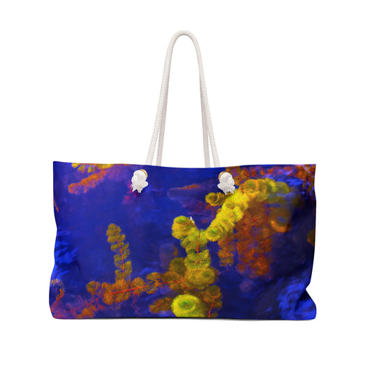A large tote bag with a vibrant yellow and purple abstract photograph printed on the exterior, with rope handles and metal grommets.