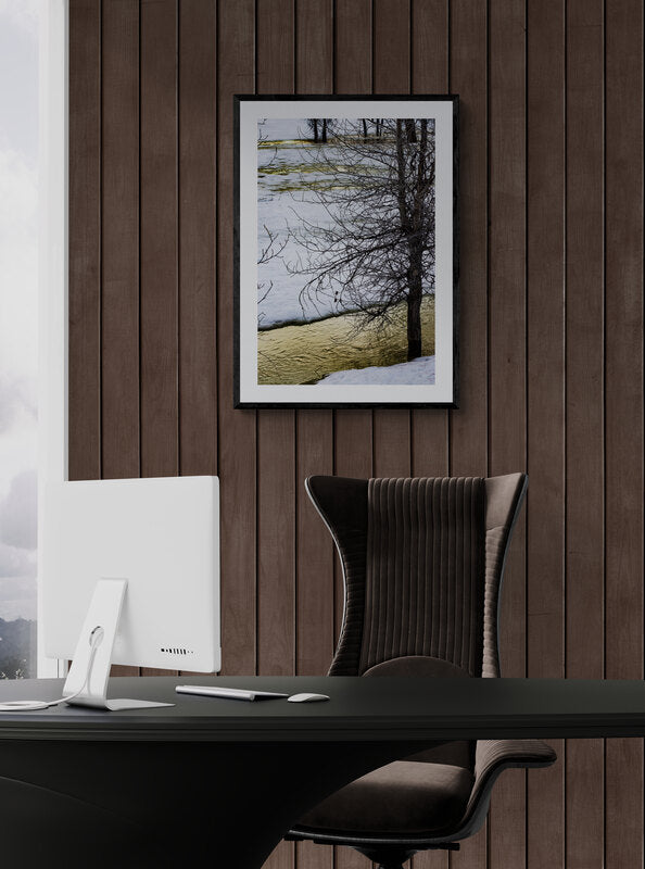 Modern office desk with a computer monitor and chair against a wooden wall with a tree picture.